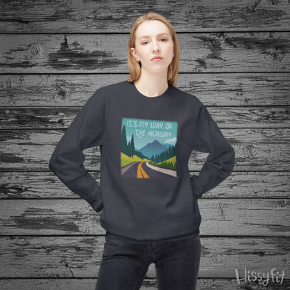 Person wearing a dark gray sweatshirt with a graphic design of a road and mountains and "It's my way or the highway" text on a wooden background